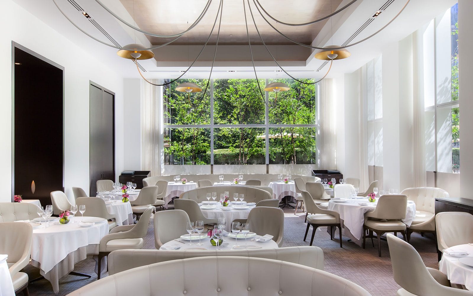Elegant romantic restaurant near Central Park with floor-to-ceiling windows, white table settings, and a bright, modern ambiance for intimate dining.