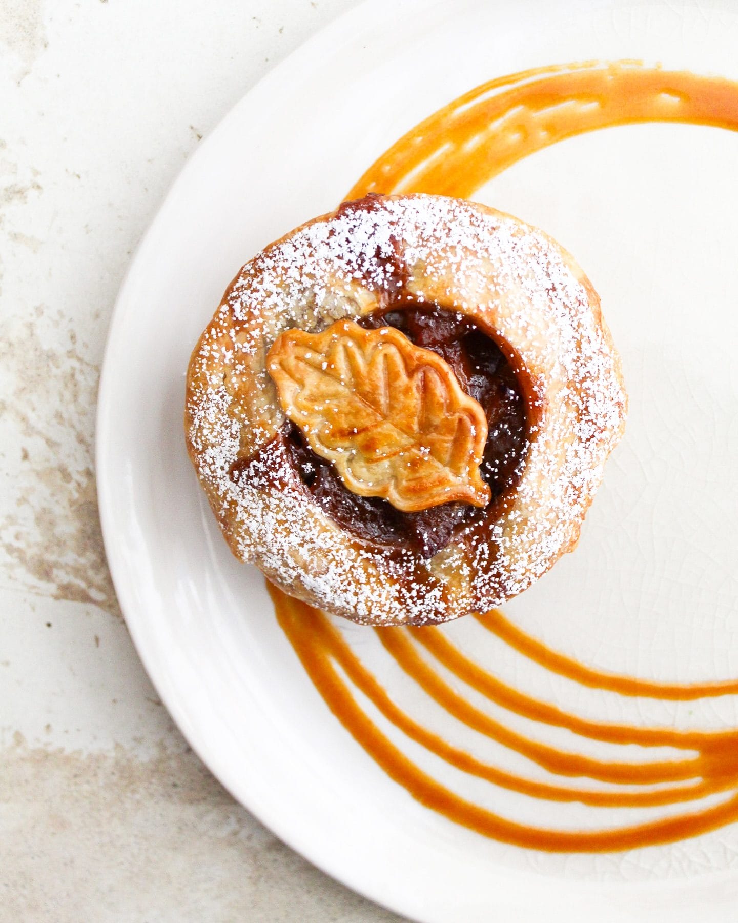 A beautifully plated dessert from ABC Kitchen, featuring a flaky pastry dusted with powdered sugar, filled with a rich filling, and topped with a decorative leaf-shaped crust. Caramel sauce is artfully drizzled on the plate, making it a budget-friendly Easter treat in a stylish setting.