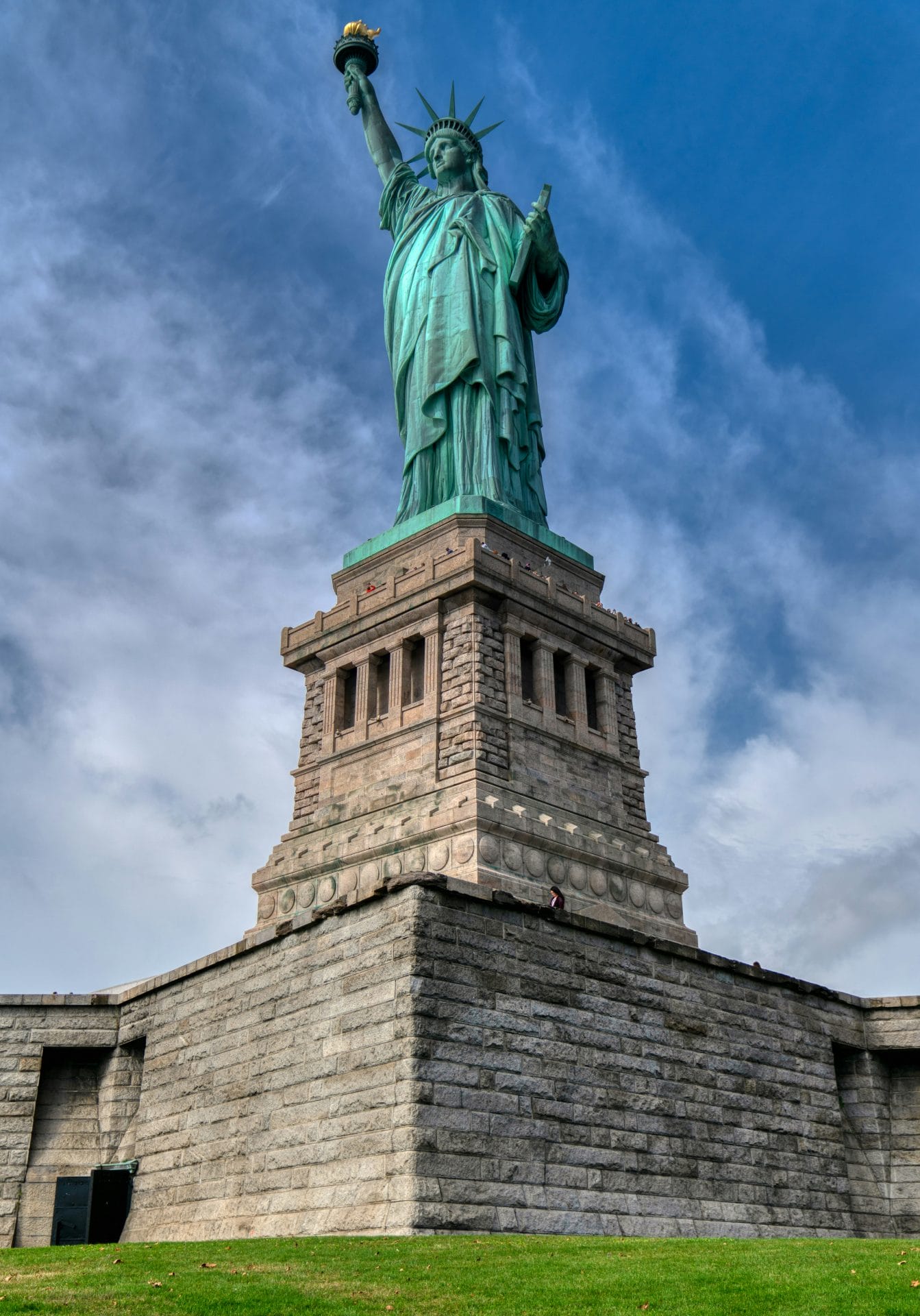 A stunning view of the Statue of Liberty proudly positioned on a lush green field. Pedestal vs. Crown Tickets