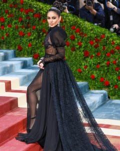 Vanessa Hudgens poses on the Met Gala 2022 red carpet wearing a sheer black lace gown with a dramatic train and statement earrings.