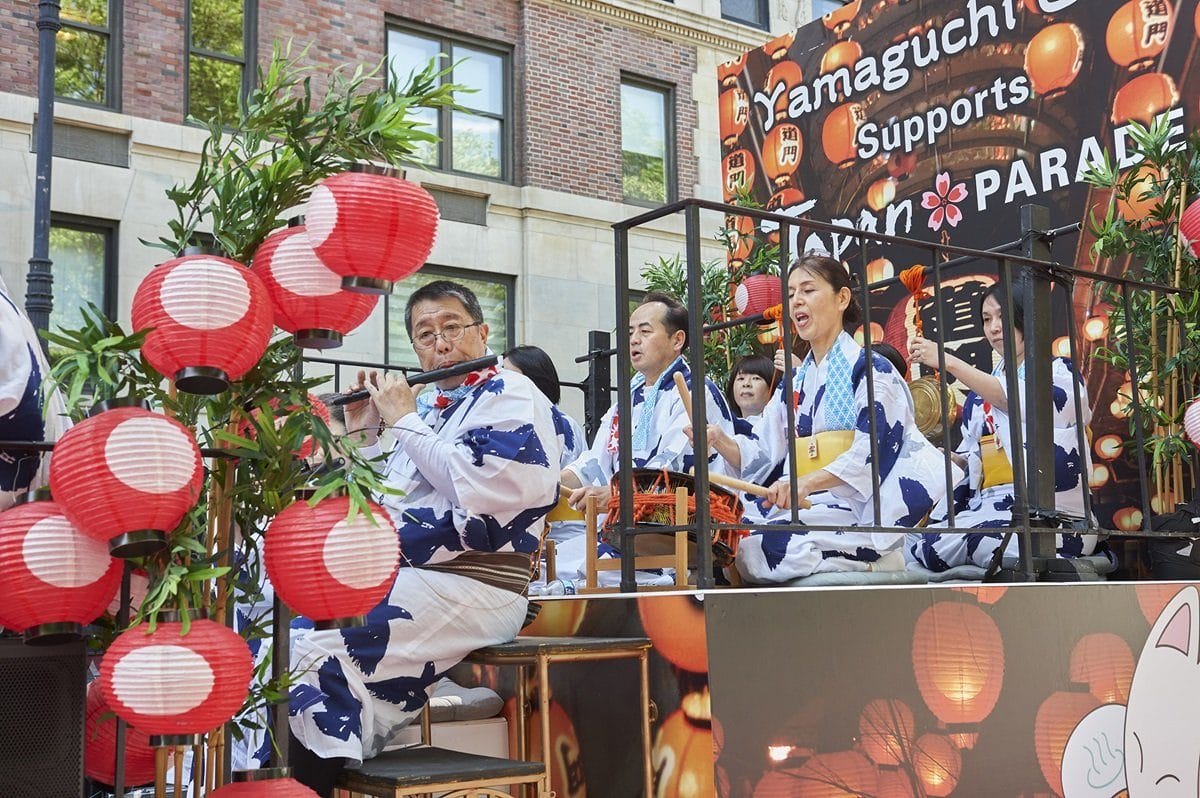 Performers in traditional Japanese attire play instruments on a float decorated with red lanterns during the Japan Day Parade & Street Fair in New York City. This image is for the blog post, "Fun Things To Do in New York This May 2025."