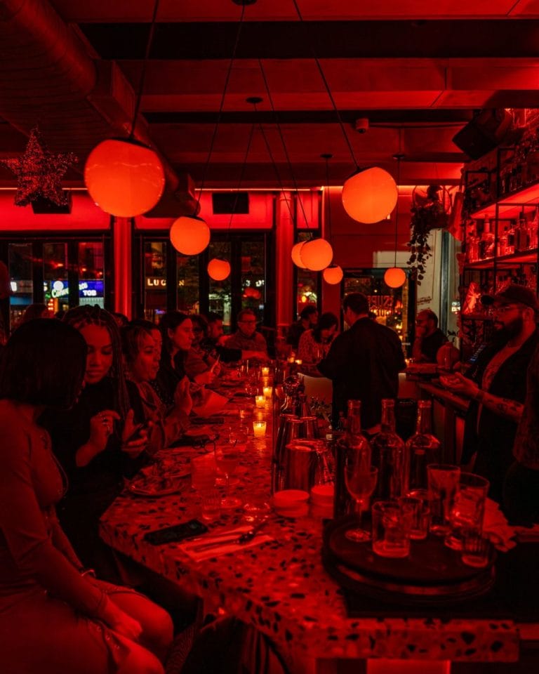 Red-lit bar with people sitting on barstools around the bar.