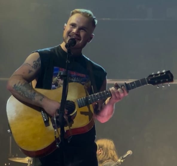 Artist Zach Bryan performing on stage with a guitar
