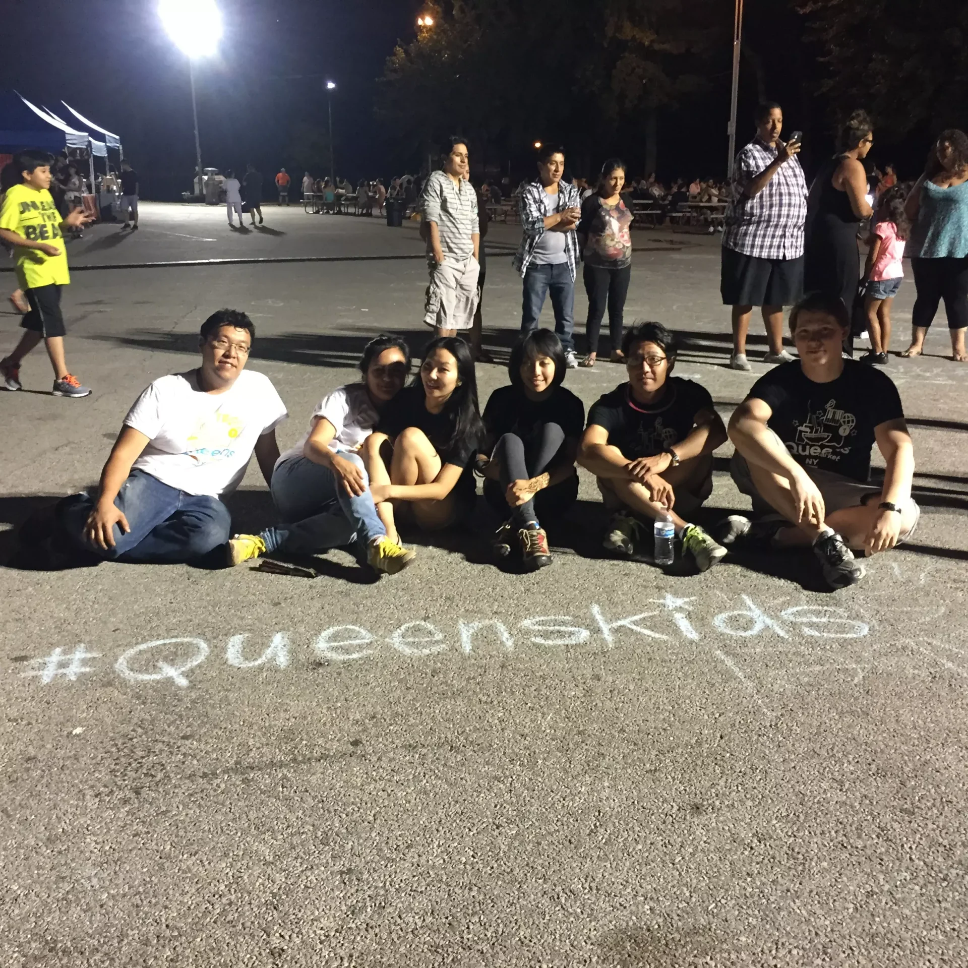 People gathering on the pavement with the passage "#Queenskids" written in chalk