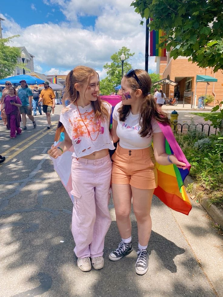 Two people wearing comfy colorful outfits while holding Pride flags.