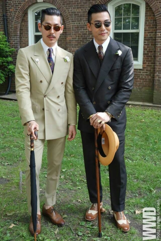 Two men dressed in 1920s attire: a suit, cane, hat, and glasses.